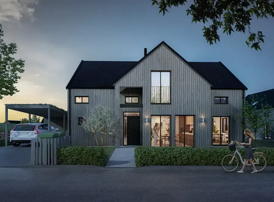 Modern villa i mörk träpanel i skymningsljus, med carport och upplysta fönster.